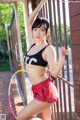 A woman in a black top and red shorts leaning against a fence.