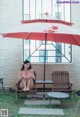 A woman sitting on a bench under an umbrella.