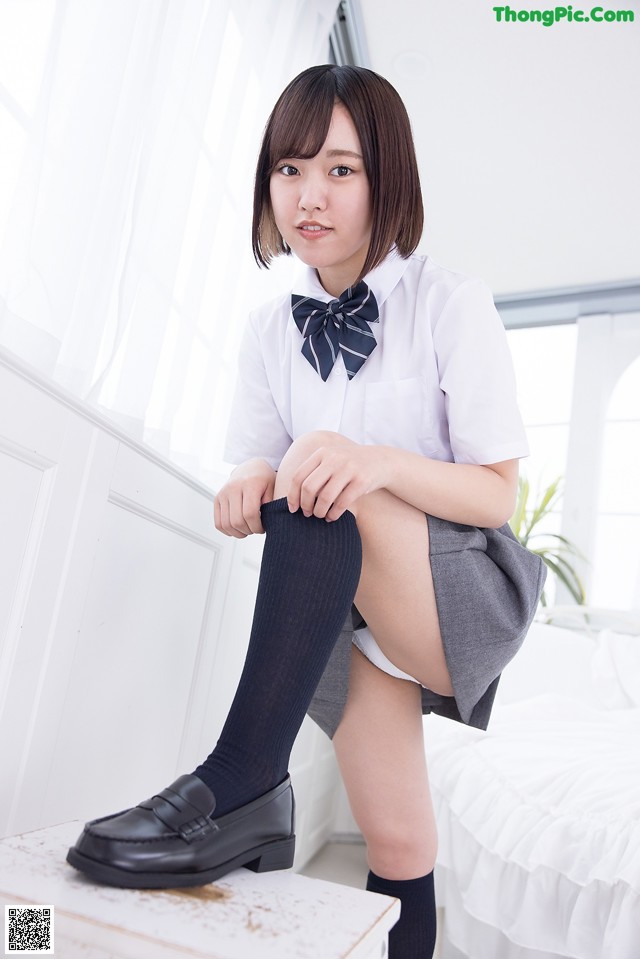 A woman in a school uniform sitting on a bed.