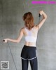 A woman in a white sports bra top and black leggings holding a skipping rope.