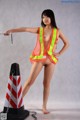 A woman in a safety vest is posing next to a traffic cone.