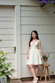 A woman in a white dress standing in front of a house.