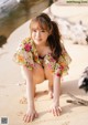 A woman in a floral dress crouching down on the beach.