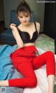 A woman in a black bra top and red pants sitting on a bed.