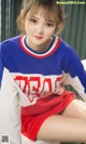 a woman sitting on top of a bed wearing a blue and red shirt