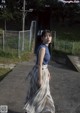 A woman in a blue top and plaid skirt walking down a sidewalk.