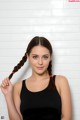 A woman in a black tank top holding her hair in a braid.