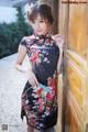 A woman in a black and red floral dress leaning against a wooden door.