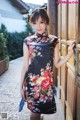 A woman in a black and red floral dress leaning against a wooden door.