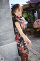 A woman in a black and red floral dress leaning against a wall.